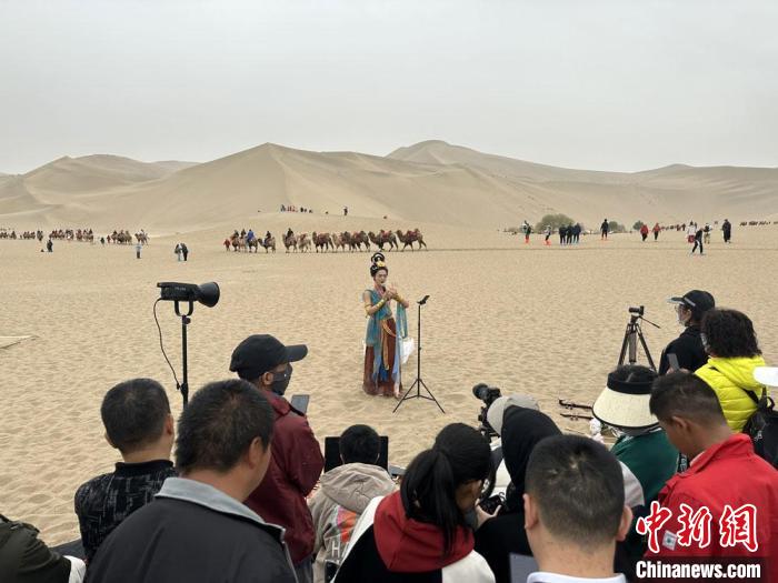 圖為2023年4月底，敦煌大漠“逐舞者”奧楠在鳴沙山月牙泉景區(qū)視頻直播，吸引游人圍觀?！●T志軍 攝